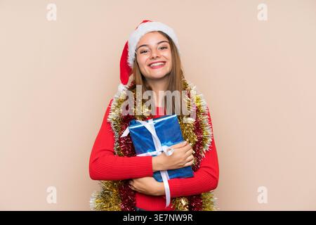 Femme hispanique portant chapeau de père noël tenant la boîte cadeau tout en se tenant debout sur fond brun dans le studio Banque D'Images