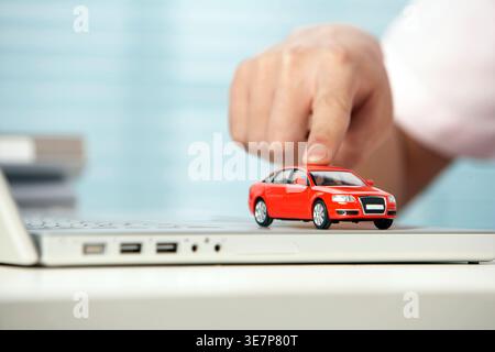 Voiture jouant à la main placée sur un ordinateur portable à l'intérieur Banque D'Images