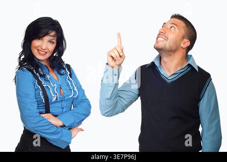 Jeune couple pose sur fond blanc. Femme sourit, bras croisés. L'homme pointe vers le haut, les yeux vers le haut. Ils semblent joyeux et ludiques. Idéal pour b Banque D'Images