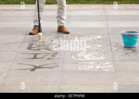 Homme chinois senior écrivant la calligraphie sur le sol dans le parc pendant la journée Banque D'Images