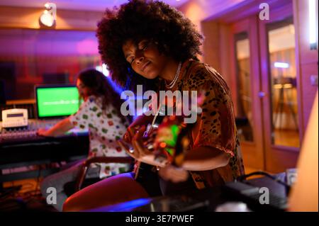 Musicienne hispanique assise et jouant de la guitare près d'un producteur de musique masculin caucasien pendant la session d'enregistrement en studio Banque D'Images
