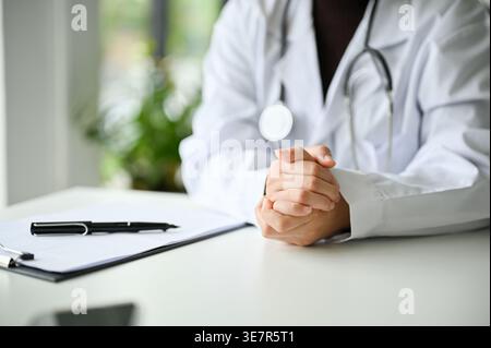 Femme asiatique médecin assise avec les mains serrées à table en clinique Banque D'Images