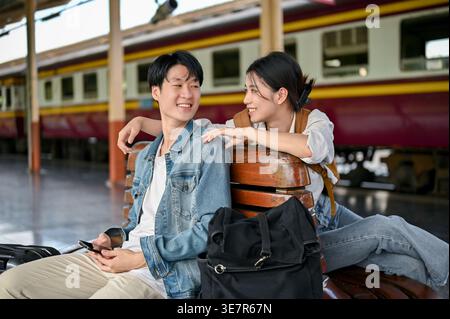 Couple de touristes asiatiques se regardant assis sur le banc dans la gare Banque D'Images