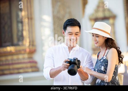 Homme chinois souriant montrant des photos capturées à son partenaire à l'aide de l'appareil photo DLSR tout en se tenant près du temple à l'extérieur Banque D'Images