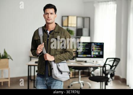 Développeur Web indien masculin avec sac bandoulière regardant loin debout dans le bureau Banque D'Images