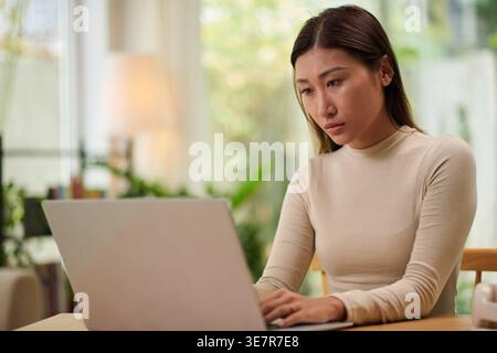 Femme asiatique travaillant sur ordinateur portable assis à table à la maison Banque D'Images