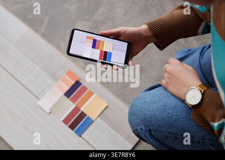 Mains de concepteur féminin mixte-race prenant photo de la palette de couleurs tout en accroupissant sur le sol dans le bureau Banque D'Images