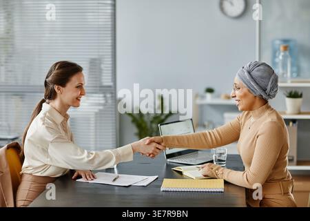 Portrait minimal de deux femmes entrepreneurs qui se secouent la main au-dessus de la table de réunion au bureau Banque D'Images