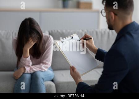 Femme du moyen-Orient penchée la tête sur la main assise devant un psychologue masculin expliquant en clinique Banque D'Images