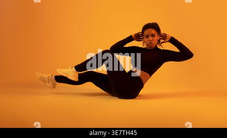 Femme noire faisant de l'exercice d'abs sur le sol sur fond orange dans le studio Banque D'Images
