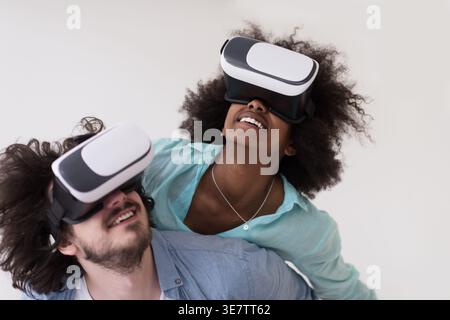 Couple noir et caucasien portant des casques VR ayant un plaisir piggyback équitation et expérimentant la réalité virtuelle sur fond blanc en studio Banque D'Images
