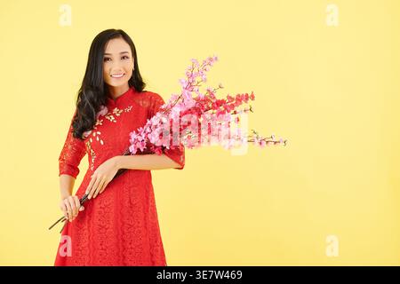 Femme asiatique tenant des branches de pêche tout en se tenant debout sur fond jaune Banque D'Images