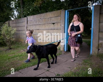 Mère avec fille promenant un chien noir à travers une porte dans un mur de béton en République tchèque Banque D'Images