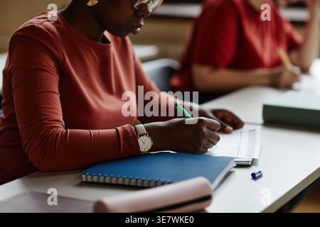 Étudiante noire concentrée écrivant sur papier prenant examen assis à table près de camarades de classe dans la classe Banque D'Images