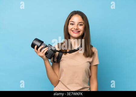 Femme hispanique tenant la caméra tout en se tenant debout sur fond bleu dans le studio Banque D'Images