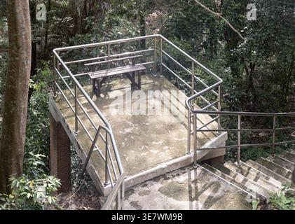 Saraburi, Thaïlande - 20 mars 2022 - Une petite plate-forme surélevée en béton avec un banc en bois surplombe une forêt dense et verdoyante. Acier inoxydable moderne s Banque D'Images