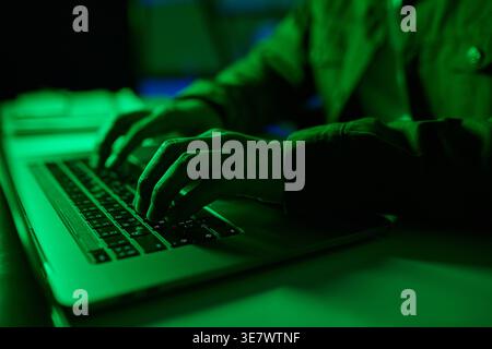 Programmeur masculin asiatique utilisant un ordinateur portable tout en étant assis à la table avec des néons verts dans le bureau Banque D'Images