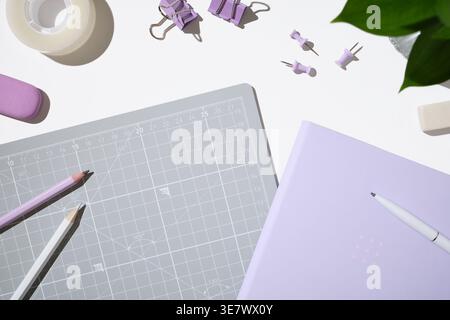 Papeterie violette et fournitures de bureau sur le bureau blanc. Carnet de notes, tapis de découpe, crayons, pinces à reliure et punaises. Espace de travail pour la planification ou la création w Banque D'Images