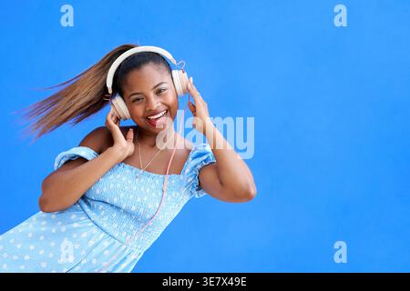 Femme hispanique joyeuse écoutant de la musique avec des écouteurs sur fond bleu Banque D'Images