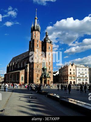Les gens se rassemblent sur la place près de l'église de Cracovie, en Pologne, sous un ciel bleu avec des nuages. La scène montre la vie urbaine et l'architecture. Banque D'Images
