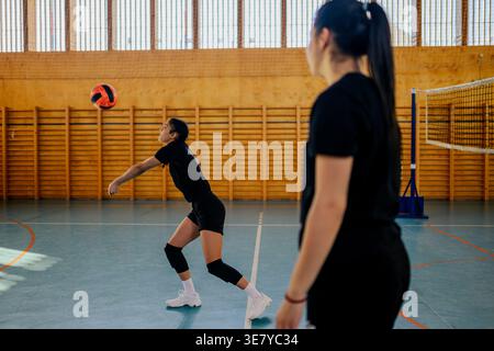 Volleyball féminin mixte recevant le ballon pendant l'entraînement avec ses coéquipières sur un terrain couvert Banque D'Images