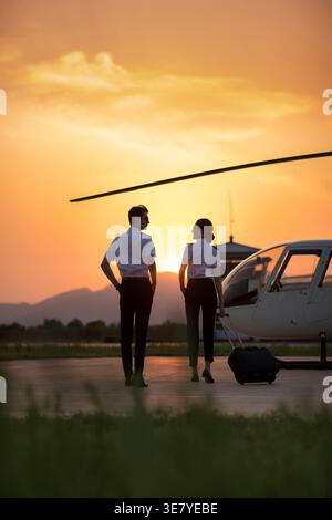 Pilotes chinois masculins et féminins debout près de l'hélicoptère pendant le coucher du soleil Banque D'Images