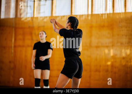 Volleyball féminin mixte recevant le ballon pendant l'entraînement avec ses coéquipières sur un terrain couvert Banque D'Images