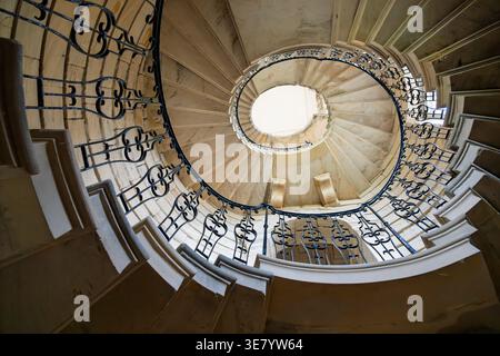 En regardant un grand escalier incurvé avec des ferronneries détaillées et une construction en pierre vieillie Banque D'Images