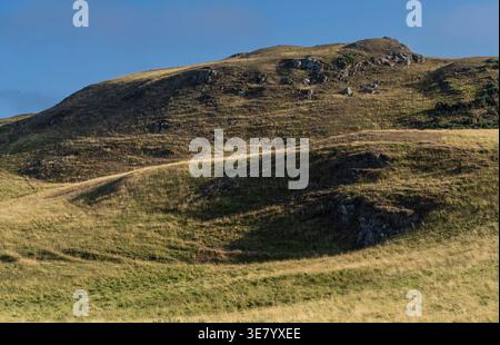 La lumière du soleil projette des ombres spectaculaires sur des collines verdoyantes et dorées sous un ciel bleu vaste et clair Banque D'Images