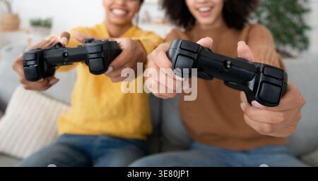 Amies noires utilisant la manette de jeu s'amusant tout en étant assis sur le canapé dans le salon à la maison Banque D'Images