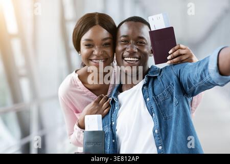 Voyageur de couple noir souriant tenant des passeports avec billet d'avion debout près les uns des autres sur la passerelle dans l'aéroport Banque D'Images