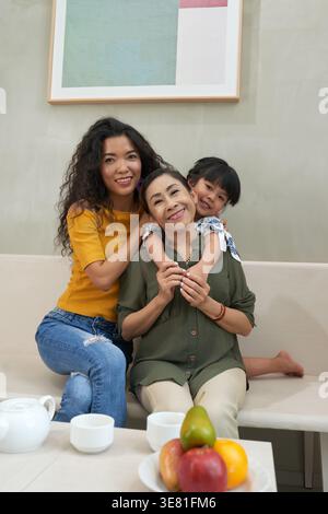 Grand-mère asiatique embrassée par sa fille et sa petite-fille assis sur le canapé ensemble à la maison Banque D'Images