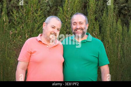 Souriant homme hispanique d'âge moyen et mari caucasien senior debout près de plantes vertes dans le jardin pendant la journée Banque D'Images