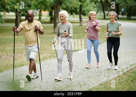 Homme noir d'âge moyen meneur courir avec des femmes âgées en utilisant des bâtons dans le parc Banque D'Images