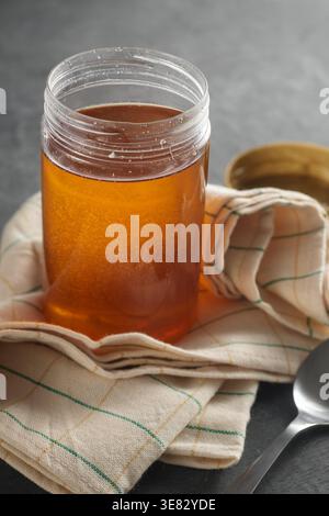 pot clair de miel avec serviette à carreaux sur la surface du dessus de table texturée sombre, édulcorant liquide dans un récipient en verre, soft focus avec espace de copie, sain Banque D'Images