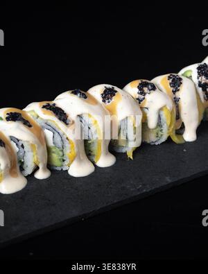 Rouleaux de sushi avec sauce crémeuse et caviar noir. L'ardoise noire offre un contraste élégant. Chaque pièce est agencée avec art, invitant les spectateurs. Parfait pour Banque D'Images