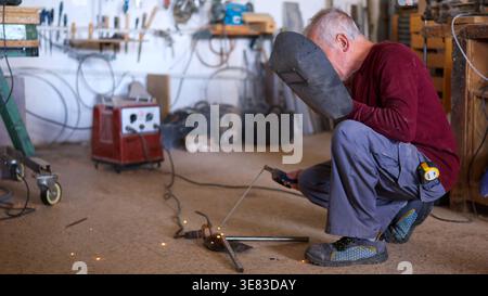 Artisan senior soudant le métal dans un atelier Banque D'Images