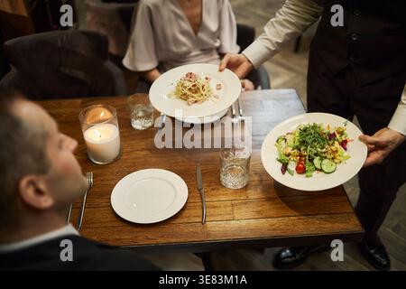 Serveur servant le dîner à un couple adulte au restaurant pour la soirée Banque D'Images