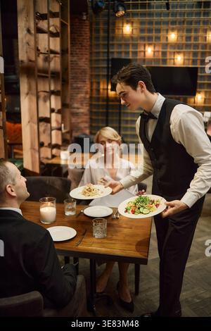 Serveur adulte servant le dîner pour couple au restaurant Hospitality Banque D'Images