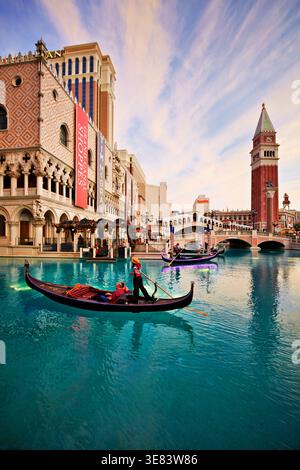 Les gondoles flottent sur l'eau devant le Venetian Hotel pendant le coucher du soleil à Las Vegas, Nevada. Les touristes apprécient la vue et la balade. Banque D'Images