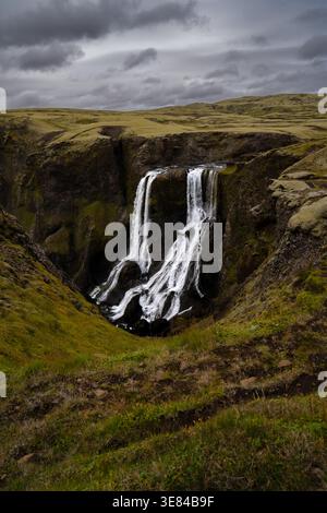 Vue sur les cascades d'eau le long d'une falaise accidentée, contrastant avec la végétation verte et le ciel spectaculaire, créant un paysage fascinant, Skaftárhrep Banque D'Images