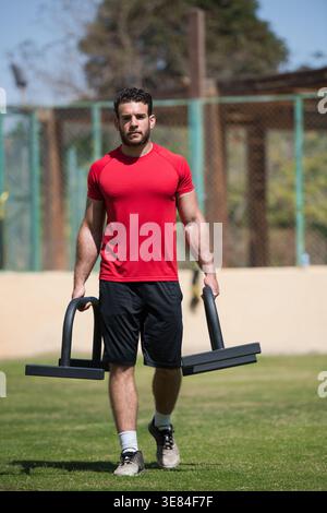 Homme arabe du moyen-Orient faisant CrossFit Farmer's Walk dans la salle de fitness en plein air avec un ami Banque D'Images