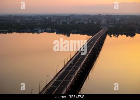 Dnipro, Ukraine, une vue surélevée d'un long pont de la ville enjambant la large rivière à l'aube du 19 mai 2023, mettant en valeur l'eau sereine reflétant le wa Banque D'Images