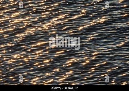 Lumière dorée scintillante sur la surface de l'eau bleu foncé de la mer Baltique créant de belles ondulations et bokeh éclatantes. Banque D'Images