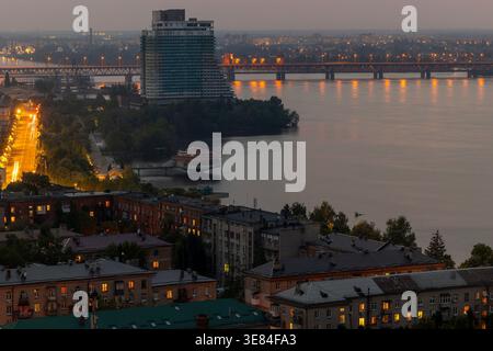 Dnipro, Ukraine, un paysage urbain serein au crépuscule capturé d'en haut, le large fleuve Dnipro reflétant les lumières de la ville, un pont en treillis proéminent, un non-nageoire imposant Banque D'Images