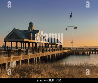 Charleston, Caroline du Sud - US - 27 mars 2026 Golden Sunrise Bathes Waterfront Park Pier à Charleston, où de longues ombres s'étendent sur l'eau calme, les drapeaux s'agitent Banque D'Images