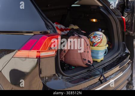 Compartiment arrière emballé de SUV sombre avec sac à dos, casque enfant et baignoire en plastique, sortie familiale, logistique routière et concept de voyage d'utilisation quotidienne Banque D'Images