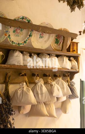 Sacs en tissu blanc remplis d'herbes séchées suspendus et assis sur des étagères en bois rustiques avec de vieilles assiettes Banque D'Images