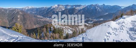 Panorama view of snowcapped mountains, from the top of a summit down into the valley floor and a frozen lake. Winter hiking and tracks in the snow. Banque D'Images