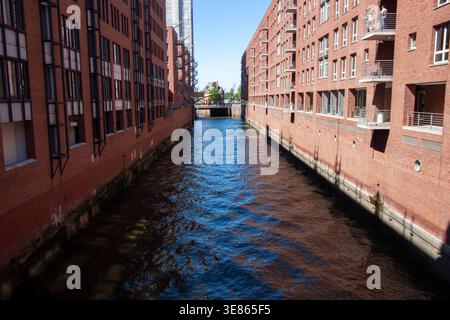 Un canal aux eaux bleu foncé entre de grands entrepôts en briques rouges et des immeubles de bureaux dans le quartier Speicherstadt de Hambourg sous un ciel bleu clair Banque D'Images